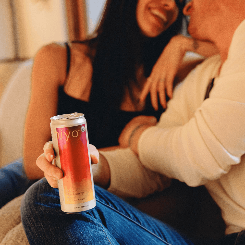 Person holding a clear can with red-to-clear gradient liquid labeled "iyo" while sitting with others.