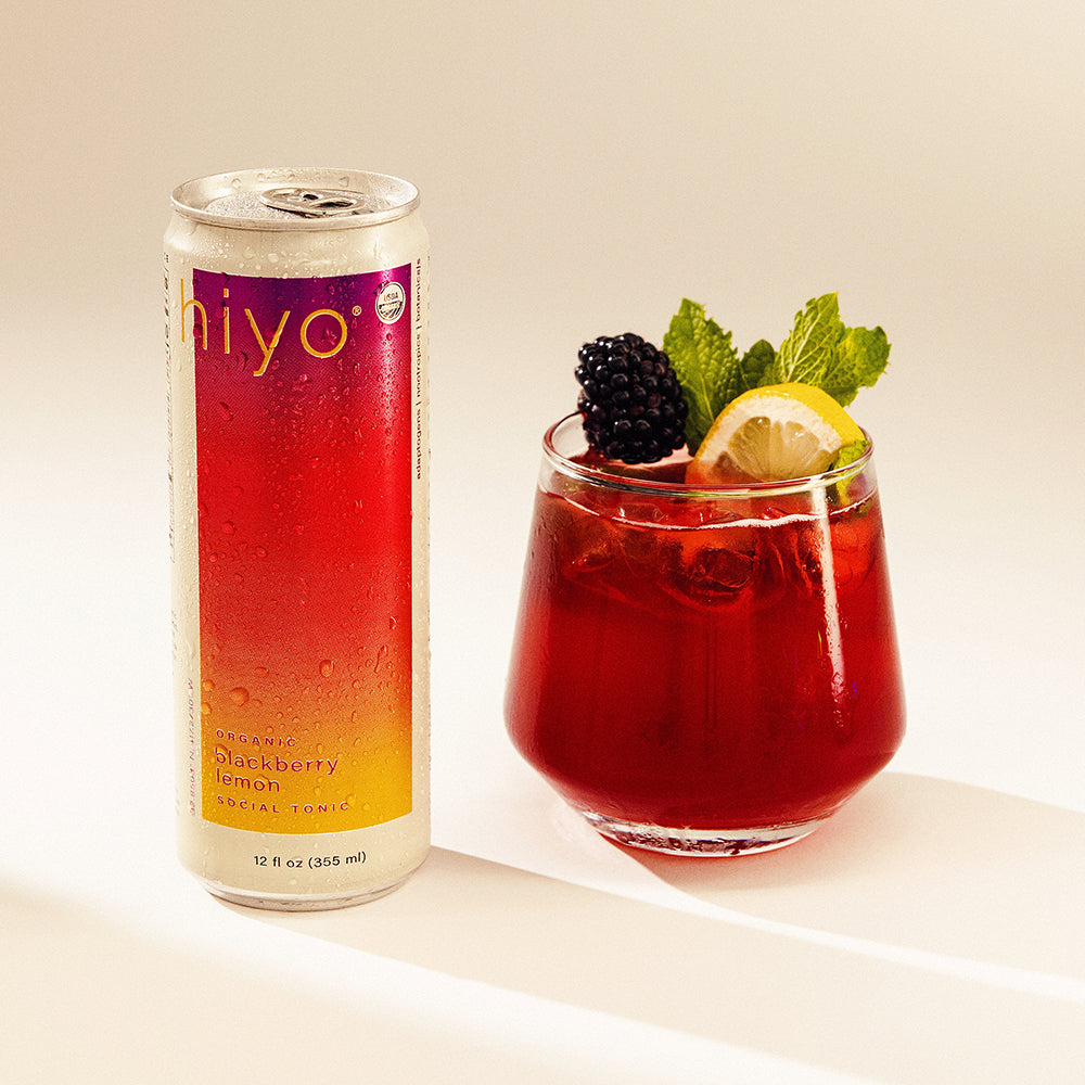 Can of hiyo blackberry lemon non-alcoholic functional seltzer hiyo next to a mocktail of the same drink with garnishes on a light background