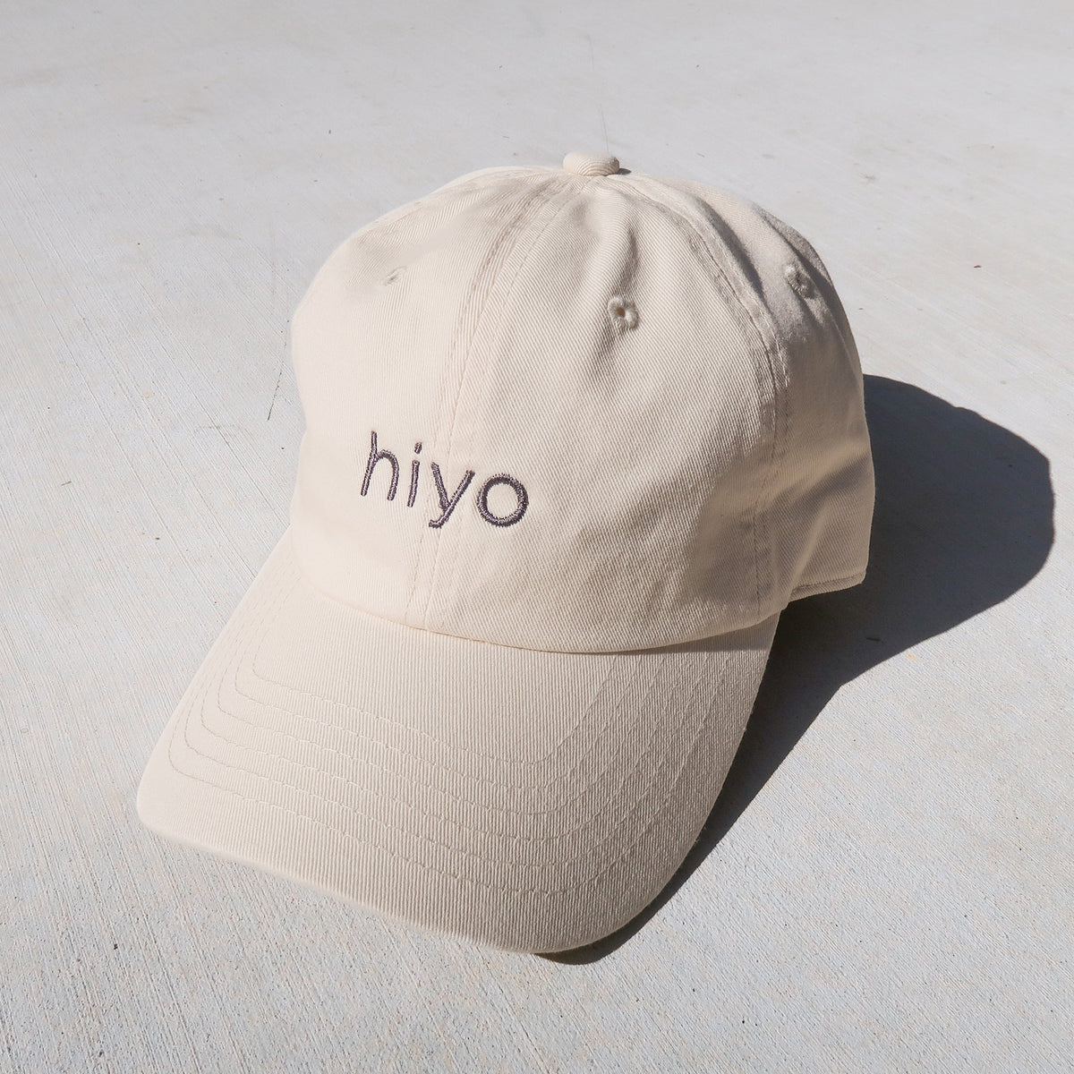a cream dad hat featuring the hiyo logo embroidered in charcoal.