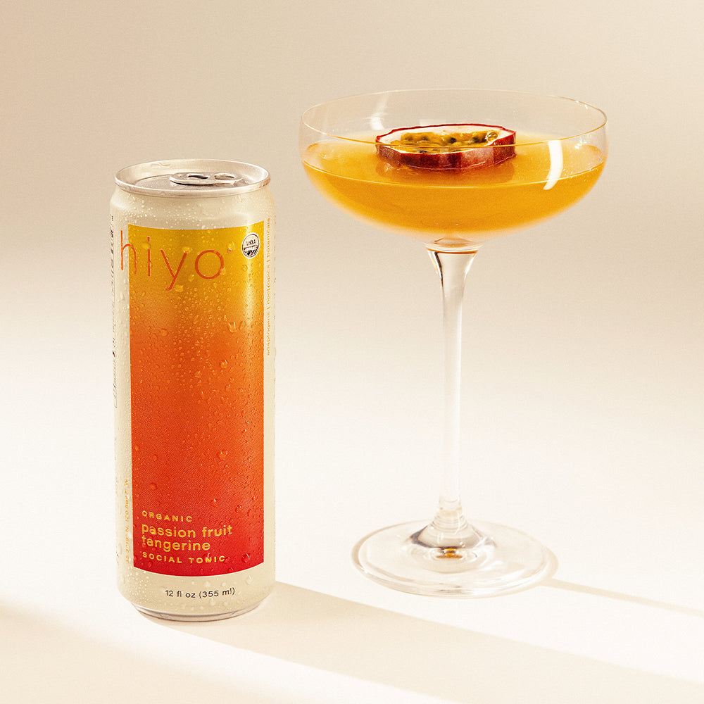 Can of non-alcoholic functional seltzer hiyo passion fruit tangerine next to a mocktail with a passion fruit slice on a light background