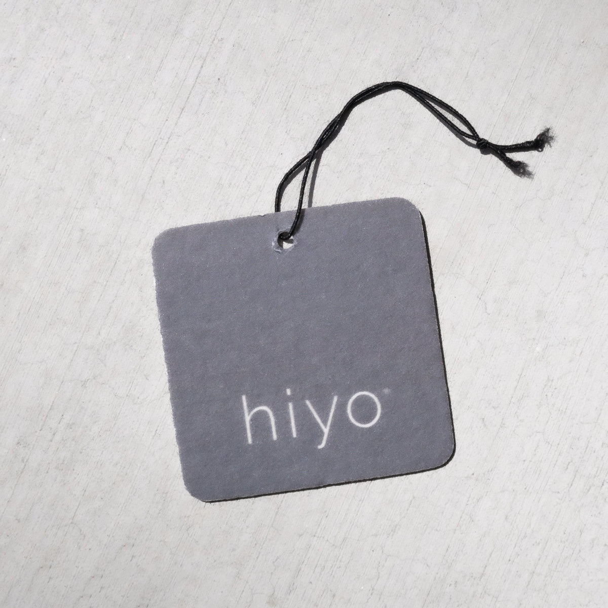 Gray square air freshener with "hiyo" text and black string attachment.