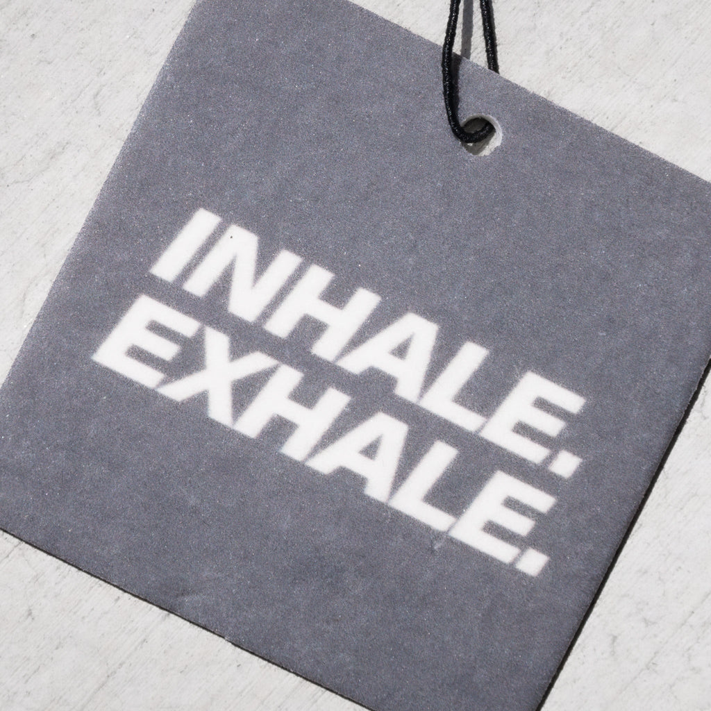 Gray rectangular air freshener tag with white "INHALE EXHALE" text and black hanging string.