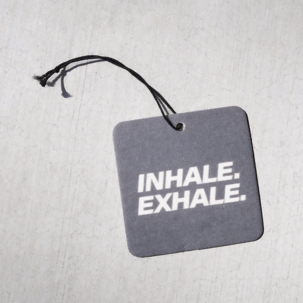 Gray square air freshener with "INHALE. EXHALE." text and black string attachment.
