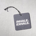 Gray square air freshener with "INHALE. EXHALE." text and black string attachment.