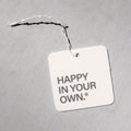 Square white air freshener tag with "HAPPY IN YOUR OWN" text, attached with black and white twine.