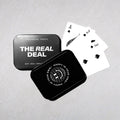 Black and white playing cards with spade suit displayed next to two metal storage tins labeled "The Real Deal" and "Happy in 
