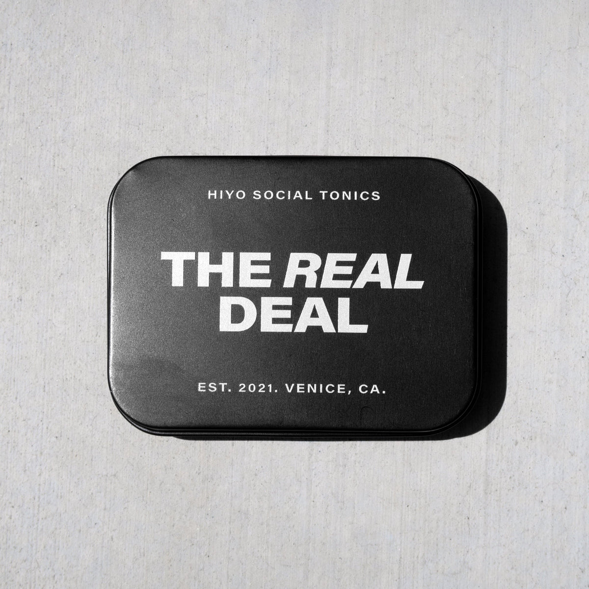 Black metal tin with white text reading "The Real Deal" and "Hiyo Social Tonics" branding, established 2021 in Venice, CA.