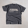 Charcoal gray t-shirt with white text reading "In The Spirit Of Being Free" and descriptive text on chest.