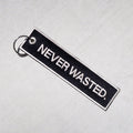 Black rectangular keychain with white border and "NEVER WASTED" text, attached to metal split ring.