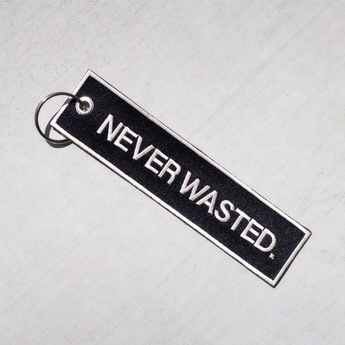 Black rectangular keychain with white border and "NEVER WASTED" text, attached to metal split ring.