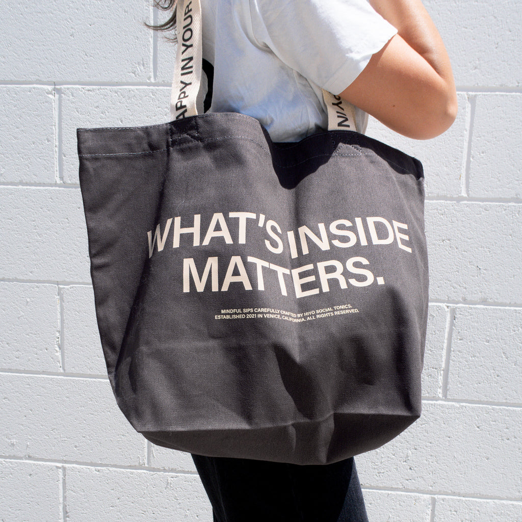 Charcoal tote bag with "WHAT'S INSIDE MATTERS" text printed in white, worn over shoulder.