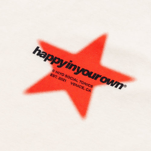 White baby tee with red star graphic and black text reading "happy in your own" with brand details.