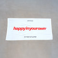 White beach towel with red "happyinyourown" text and tagline printed on front.