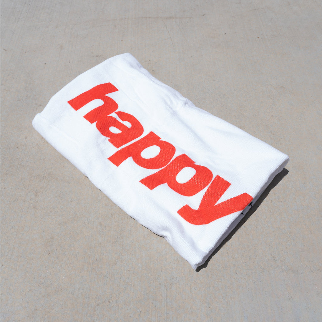 White beach towel with large red text reading "HAPPY" printed on front.