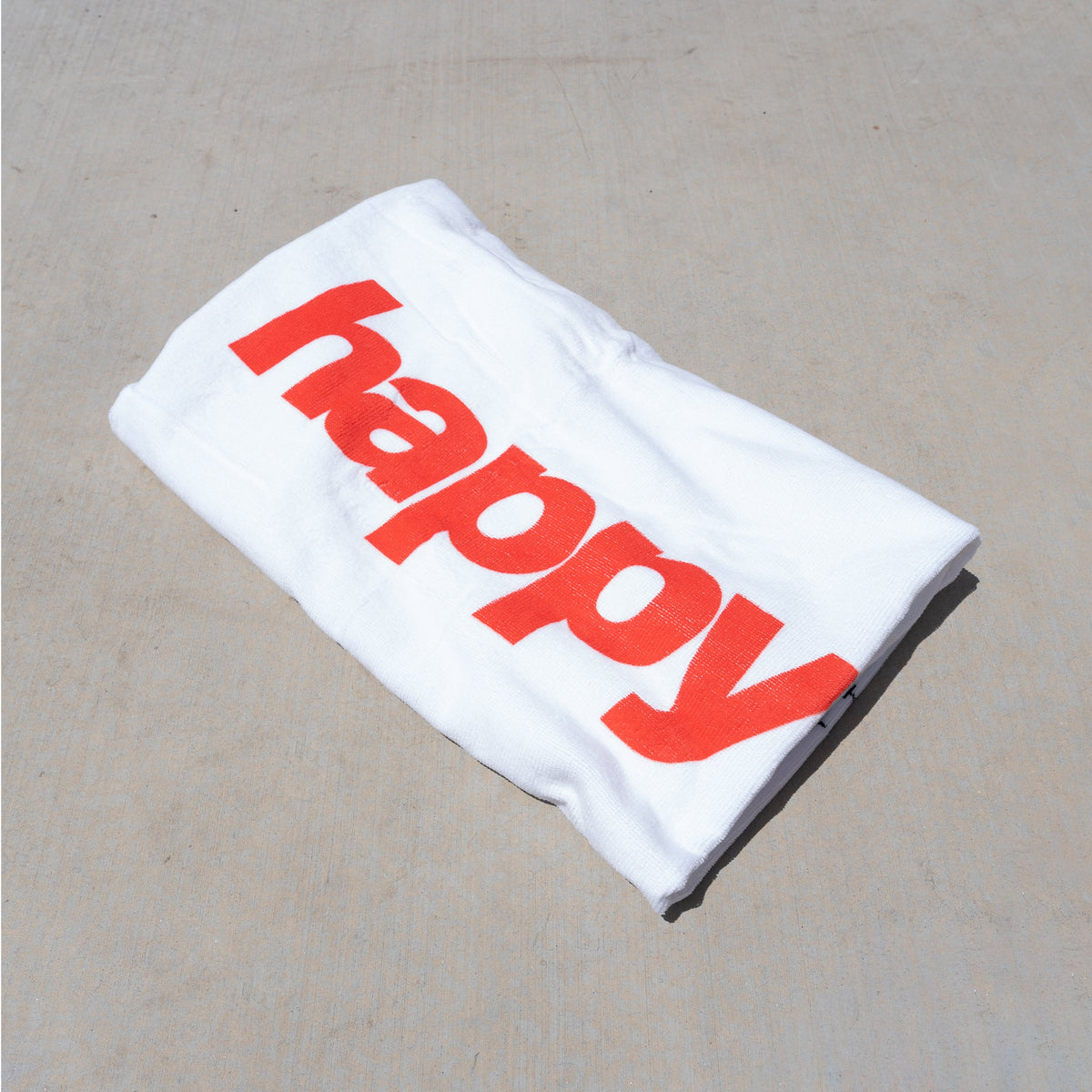 White beach towel with large red text reading "HAPPY" printed on front.