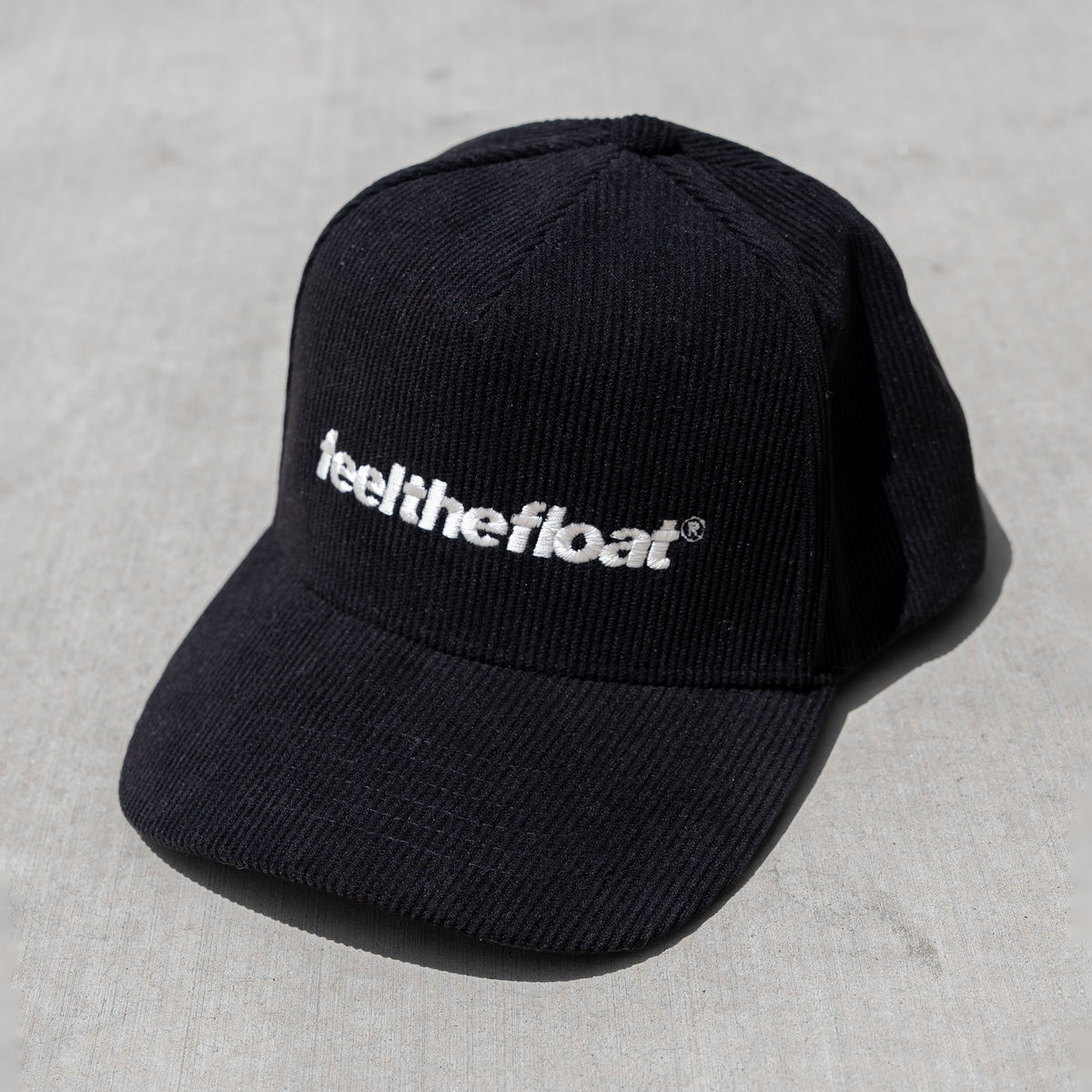 Black trucker hat with white "feel the float" text embroidered on the front.