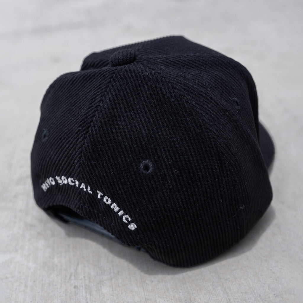 Black trucker hat with ribbed fabric, mesh back panels, and white embroidered text on side.
