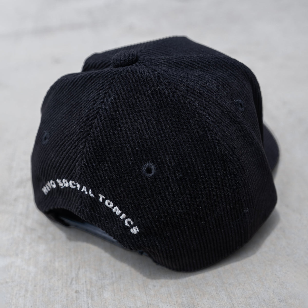 Black trucker hat with ribbed fabric, mesh back panels, and white embroidered text on side.