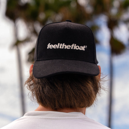 Black trucker hat with "feel the float" embroidered text on front and mesh back panels, shown from rear view on wearer.