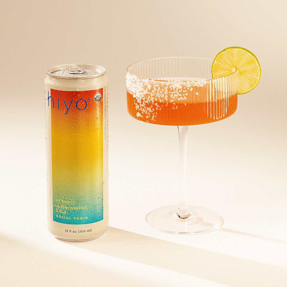 Can of non-alcoholic functional seltzer hiyo sparkling watermelon lime tonic next to a glass with a lime wedge on a light background