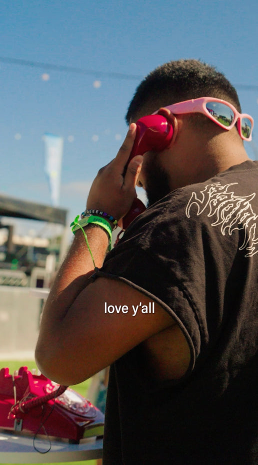 people at an outdoor festival pick up a vintage red telephone at a hiyo activation and respond to questions about what makes them feel happy in your own. the video features candid interviews, vibrant festival fashion, drinks in hand, and a lively atmosphere with on-screen captions highlighting their responses.