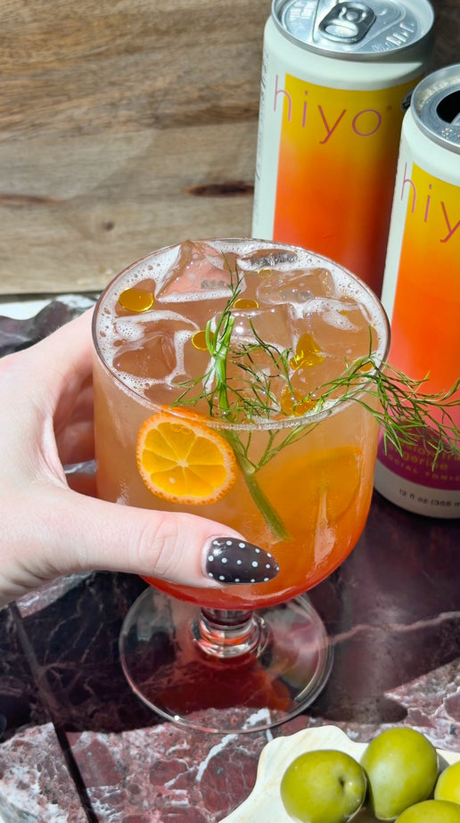 a close-up of hiyo passion fruit tangerine social tonic cans arranged on a marble table in warm sunlight. the video features a recipe using fresh citrus, fennel syrup, and passion fruit tangerine hiyo that highlights the beverage in a bright, elevated setting.