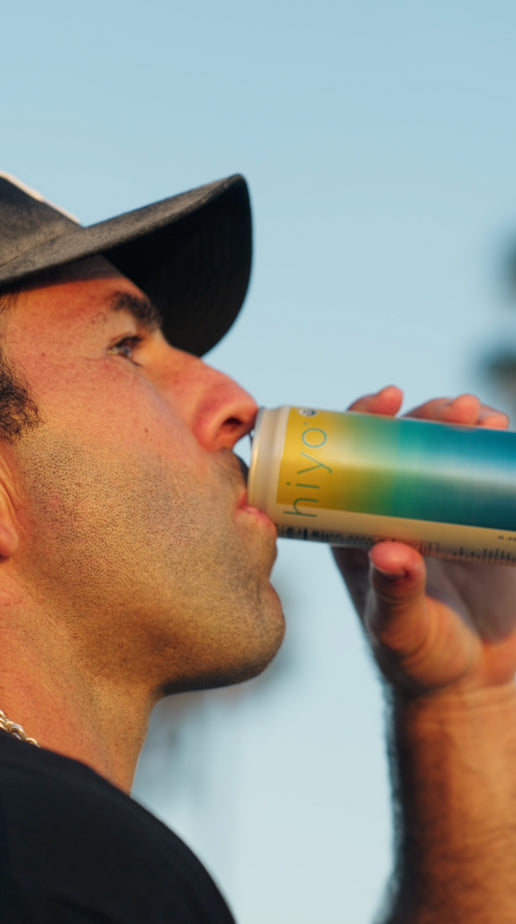 a soccer freestyler performs tricks with a yellow soccer ball along a sunny beach path while holding a can of hiyo social tonic. the video features fast-paced footwork, juggling, and scenic palm-lined views before ending at sunset with the athlete relaxing and enjoying the drink.